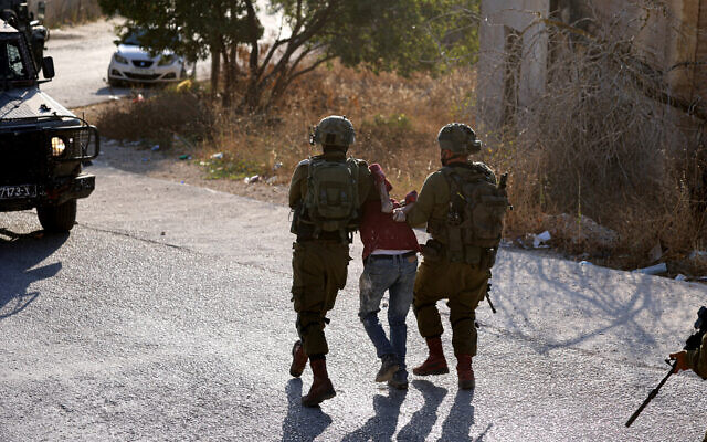 Illustrative: Israeli soldiers arrest a Palestinian man during a search operation in the West Bank village of Baita, August 21, 2023. (Jaafar Ashtiyeh/AFP)