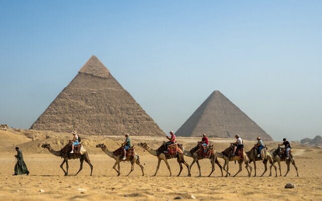 A guide pulls a lead camel as tourists ride in a row past the Great Pyramid of Khufu (Cheops, R) and the Pyramid of Khafre (Chephren, L) at the Giza Pyramids Necropolis on the outskirts of Giza on May 3, 2024. (Jewel SAMAD / AFP)