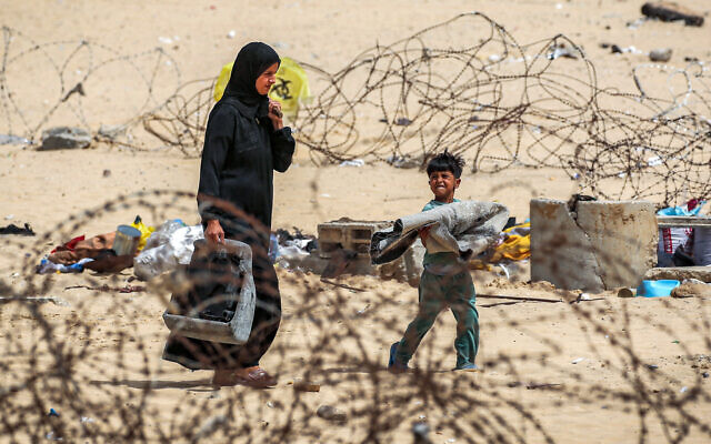 A woman and boy walk with belongings past barbed-wire fences as they flee from Rafah in the southern Gaza Strip on May 11, 2024, during the ongoing conflict in the Palestinian territory between Israel and terror group Hamas. (AFP)