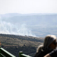 Illustrative: People watch as smoke rises at the site of a rocket strike from Lebanon on the Golan Heights on May 17, 2024. (Jalaa Marey/AFP)