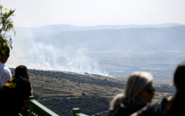 Illustrative: People watch as smoke rises at the site of a rocket strike from Lebanon on the Golan Heights on May 17, 2024. (Jalaa Marey/AFP)