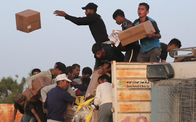 Palestinians carry boxes of humanitarian aid after rushing the trucks transporting the international aid from the US-built Trident Pier near Nuseirat in the central Gaza Strip on May 18, 2024. (AFP)