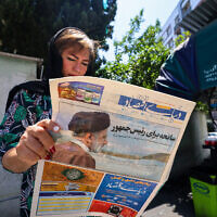 A woman reads a newspaper with a front-page report on the crash of the Iranian president's helicopter outside a kiosk in Tehran on May 20, 2024. (Atta Kenare / AFP)
