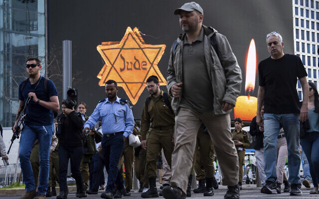 People walk next to a billboard showing a yellow Star of David that reads 'Jude,' Jew in German, resembling the one Jews were forced to wear by Nazis, during the annual Holocaust Remembrance Day in Tel Aviv, Israel, May 6, 2024 (AP Photo/Oded Balilty)