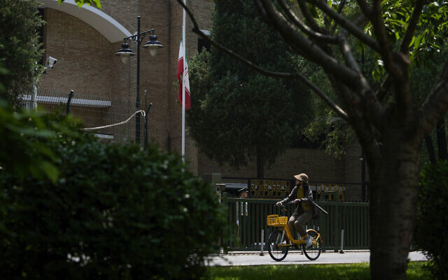 A woman cycles past an Iranian national flag set to half staff to mourn the death of President Ebrahim Raisi, at the Iran embassy in Beijing, Monday, May 20, 2024.  (AP Photo/Andy Wong)
