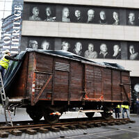 Portraits of Holocaust survivors displayed at the Museum of Jewish Heritage as a vintage German train car, like those used to transport people to Auschwitz and other death camps, sits on tracks outside the museum, in New York, Sunday, March 31, 2019. (AP/Richard Drew)