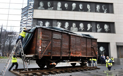 Portraits of Holocaust survivors displayed at the Museum of Jewish Heritage as a vintage German train car, like those used to transport people to Auschwitz and other death camps, sits on tracks outside the museum, in New York, Sunday, March 31, 2019. (AP/Richard Drew)