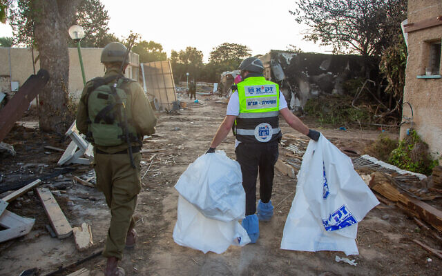 ZAKA volunteers walk through the destruction caused by Hamas terrorists in Kibbutz Kfar Aza, as they collect dead bodies, October 15, 2023. (Edi Israel/ Flash90)
