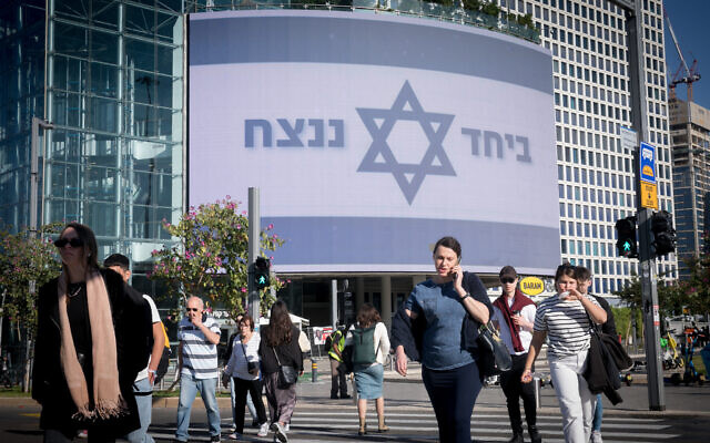 People walk by a large billboard reading "Together we will win" at the Azrieli shopping mall in Tel Aviv. December 19, 2023. (Miriam Alster/Flash90)