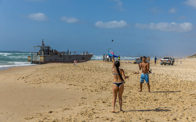 Israelis stand near a US Army vessel that washed up on a beach in Ashdod, May 25, 2024. (Liron Moldovan/Flash90)
