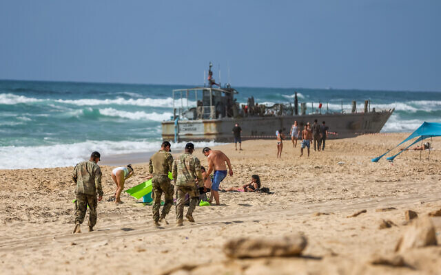American soldiers and Israelis stand near a US vessel that washed up on the beach in Ashdod, May 25, 2024. (Liron Moldovan/Flash90)