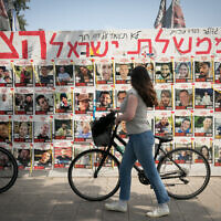 People walk by photographs of  people still held hostage by Hamas terrorists in Gaza, at Hostage Square in Tel Aviv. May 1, 2024. (Miriam Alster/Flash90)