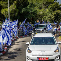 People wave the Israeli flag as they pay their respect to counter-terror officer Arnon Zamora, who was killed in battle on June 8 during a special operation to rescue four Israeli hostages from Gaza, outside his family home in Mevasseret Zion, June 9, 2024.  (Yonatan Sindel/Flash90)