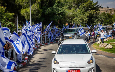People wave the Israeli flag as they pay their respect to counter-terror officer Arnon Zamora, who was killed in battle on June 8 during a special operation to rescue four Israeli hostages from Gaza, outside his family home in Mevasseret Zion, June 9, 2024.  (Yonatan Sindel/Flash90)